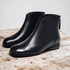 Pair of black leather ankle boots with round toe and low metallic heel on wooden table
