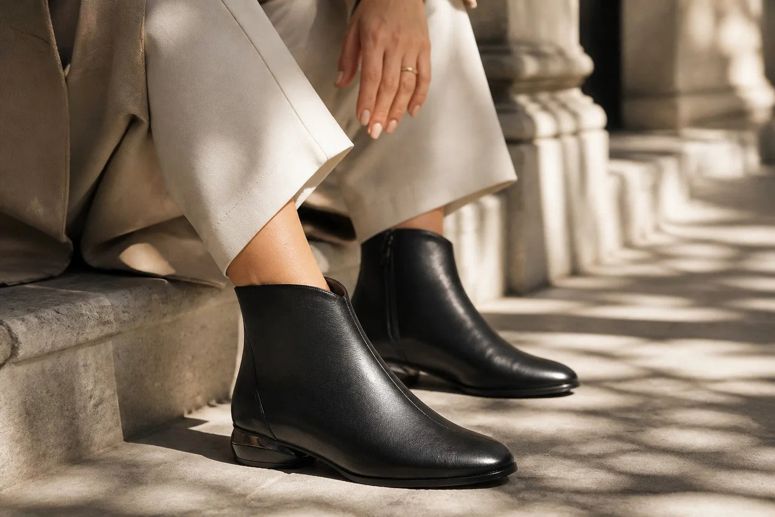 Close-up of black ankle boots with back zip detail worn with white trousers
