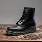 Side view of black leather lace-up combat boot with yellow stitched sole on wooden surface