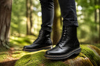 Close-up of black leather boots worn with cuffed black jeans while standing on mossy rock outdoors
