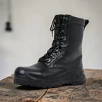 Side view of a tall black leather combat boot with lace-up front, standing on a rustic wooden table.