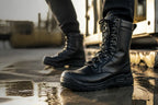 Side profile of black leather combat boots in motion on a wet industrial surface with lace detail visible.