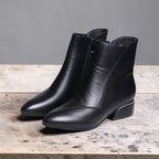 Pair of black leather ankle boots with pointed toe and side zip shown on a wooden surface