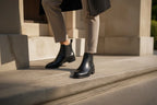 Close-up of a woman's legs wearing black leather Chelsea boots while stepping up stone stairs in tailored trousers